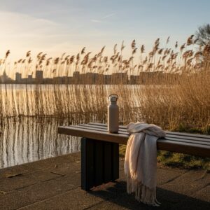 Rustige avondsetting bij water en riet in Den Haag met bankje, herbruikbare fles en sjaal; minimalistische wellness-sfeer die balans en mindful herstel uitstraalt binnen orthomoleculaire begeleiding