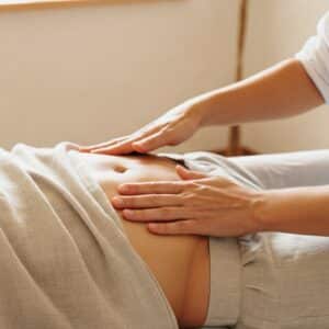 Close-up van handoplegging op de buik tijdens een Reiki-behandeling, met warm daglicht in een praktijk in Geldrop, gericht op energetisch herstel.