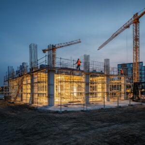 Een moderne bouwplaats in Hoofddorp bij schemering, met helder verlichte gebouwen in aanbouw, symbool voor het opbouwen van een sterke basis voor gezondheid en welzijn.