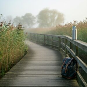 Othomoleculair therapeut Dordrecht – mistige ochtend in de Biesbosch met houten boardwalk tussen riet, rugzak en thermos; kalme natuur als steun voor herstel en balans.