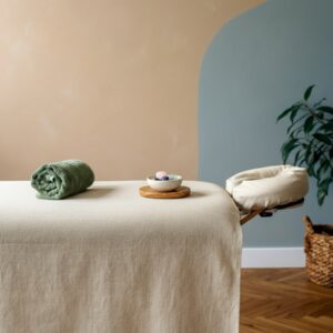 Minimalistische Reiki-studio in Hoofddorp met massagebank, opgevouwen sage handdoek, kristallen en een plant in zacht daglicht; rustgevend detail voor Reiki Hoofddorp